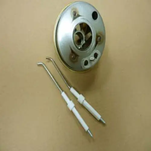 Metallischer Zentrierstern mit einem Flammkopf, zwei gebogenen Werkzeugen in der Nähe. Produktelement von Remeha, auf braunem Hintergrund platziert.